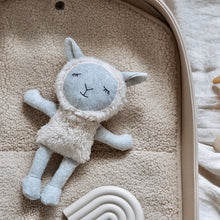 Load image into Gallery viewer, Gray-and-cream fabric sheep doll with a fluffy textured body, black embroidered sleepy eyes, and soft gray limbs, displayed lying down on a beige textured blanket inside a rounded fabric tray beside  a neutral-colored rainbow toy. 