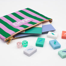Load image into Gallery viewer, Pink and green striped Mahjong accessory bag with a gold zipper and a pink rectangular patch with "MAHJ" on it, shown opened with colorful Mahjong tiles, dice, and scorecards on a white surface. 