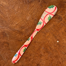 Load image into Gallery viewer, A white canapé knife with a red and green mistletoe design on a brown wooden surface.