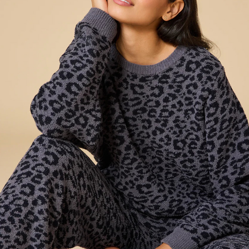 Person in a seated pose wearing a soft gray lounge set with a black leopard print pattern, shown against a soft beige background. 