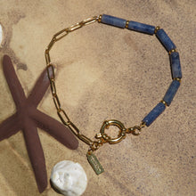Load image into Gallery viewer, Bracelet with blue beads and gold chain on a beach background.