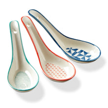 Load image into Gallery viewer, White stoneware Geo Soup spoons with red, blue, and teal rims and geometric patterned interiors, displayed on a white background.