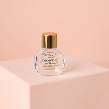 Load image into Gallery viewer, Mini Snowdrop eau de parfum in a clear glass bottle with a gold cap, shown on a powder pink pedestal and background. 