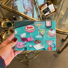 Load image into Gallery viewer, Art print featuring illustrated cocktail glasses, olives, makeup items, and a dessert on a teal background, shown held in hand in front of gold bar cart.