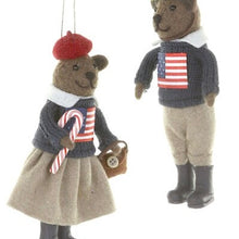 Load image into Gallery viewer, Preppy Bears Ornaments, two brown teddy bear ornaments wearing navy knit sweaters with American flag designs, white collars, and dark boots, with the girl bear in a red beret and beige skirt holding a striped candy cane and brown handbag, and the boy bear in beige trousers, suspended against a white background.