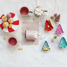 Load image into Gallery viewer, Festive flat lay with stoneware tree-shaped bowls in red, yellow, green, and purple filled with candies, surrounded by mugs, marshmallows, and cupcakes displayed on a red-and-white peppermint-striped plate, with small bottle-brush trees on a white textured surface.  