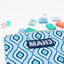 Load image into Gallery viewer, Light and dark blue geometric-patterned Mahjong accessory bag with a gold zipper and a navy rectangular patch with "MAHJ" on it, displayed with colorful Mahjong tiles, dice, and score cards on a white surface.