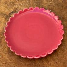 Load image into Gallery viewer, A red ceramic plate with a scalloped edge on a brown wooden surface.