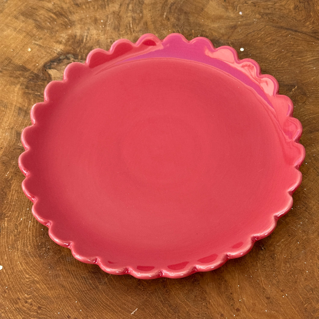 A red ceramic plate with a scalloped edge on a brown wooden surface.