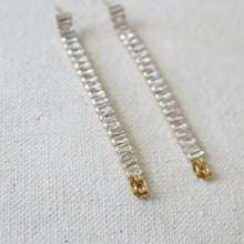 Load image into Gallery viewer, Pair of gold IP-plated earrings featuring straight rows of clear baguette-cut CZ stones with small gold end caps, displayed on a white soft textured background.