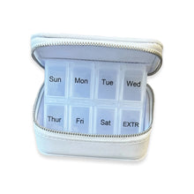 Load image into Gallery viewer, Opened light gray travel pill box revealing a weekly pill organizer labeled Sunday- Saturday in black text with an extra compartment, displayed on a white background. 