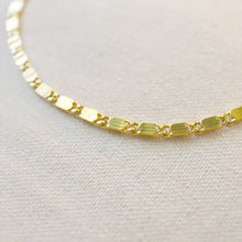 Load image into Gallery viewer, Ion-plated gold-plated brass casted bar chain necklace with reflective, light-catching links, displayed on a soft white textured b background. 