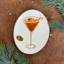 Load image into Gallery viewer, White, oval, ceramic dish with a chocolate martini design. A red and white candy cane and a brown star inside of glass. A green olive next to the glass. On a wooden surface , surrounded by fir tree cuttings. 