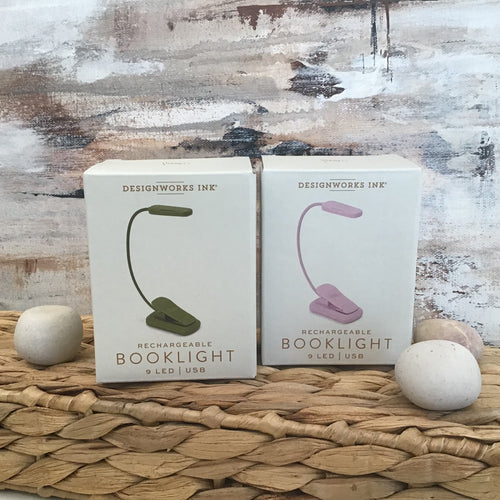 Two white boxes side by side with reading light clips on the front. The boxes are on a wicker stand with pebbles to the side of them. Abstract background. 