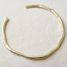 Load image into Gallery viewer, Over-head view of a 14K gold double semi-matte plated brass choker necklace with a gently uneven, organic shape displayed on a cream woven fabric surface. 