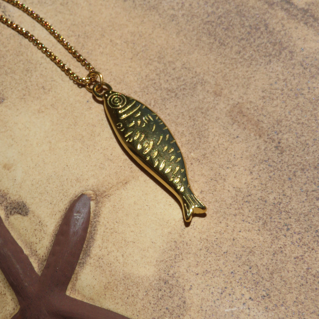 Gold fish-shaped pendant on a chain against a beige background