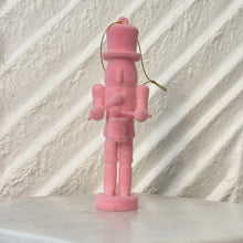 Load image into Gallery viewer, Pink nutcracker ornament holding a small drum and drumsticks, standing upright with a gold hanging cord against a white textured background. 
