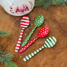 Load image into Gallery viewer, A red and white striped stainless steel spoon. A green stainless steel spoon with white polka dots. A red stainless steel spoon with white polka dots. A green and white striped stainless steel spoon. On a brown wooden surface with green fir tree cuttings , and a white ceramic pot with a red cottage, trees, and botanical motif.