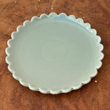 Load image into Gallery viewer, A white ceramic plate with a scalloped edge on a brown wooden surface.