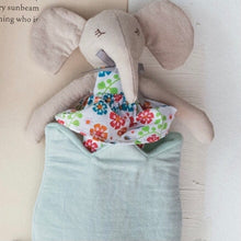 Load image into Gallery viewer, A white plushie elephant in a colorful dress , in a blue tulip bag on an opened book.