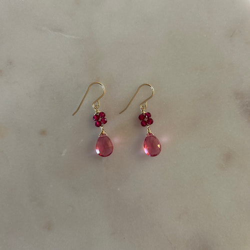 Gold drop earrings with four magenta beads and a pink teardrop gem. White marble background. 