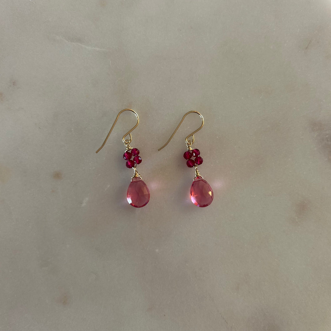 Gold drop earrings with four magenta beads and a pink teardrop gem. White marble background. 