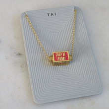 Load image into Gallery viewer, Gold-plated rectangular spinner pendant necklace with red enamel featuring the words "COUP DE FOUDRE," suspended on a gold-plated chain and displayed on a light gray TAI jewelry card on a white marble background. 
