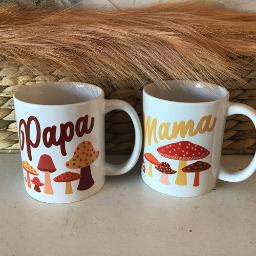 A pair of white coffee mugs with spotted mushrooms printed on them. One reads 