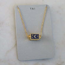 Load image into Gallery viewer, Gold-plated spinner pendant necklace with a navy enamel charm featuring a sparkly crescent moon and golden star accents, displayed on a light gray TAI jewelry card, displayed on a white background. 