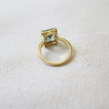 Load image into Gallery viewer, Double gold-plated brass ring shown from behind, featuring a raised rectangular emerald-cut green tourmaline spinel stone in a four-prong setting, displayed on a soft textured surface. 