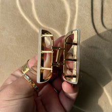 Load image into Gallery viewer, Ivory half-moon metal claw clip with gold hardware held in a hand against a beige textured surface with soft curved light reflections. 