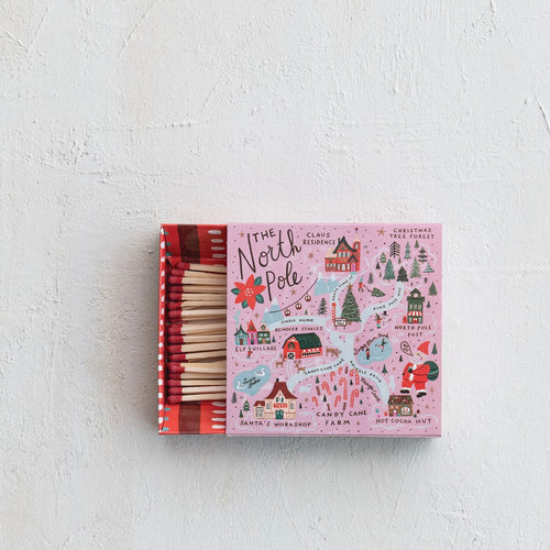 Pink matchbox with illustrated North Pole map featuring Santa, Christmas trees, candy canes, reindeer stables, and festive buildings. Red-tipped matches visible on the left side.