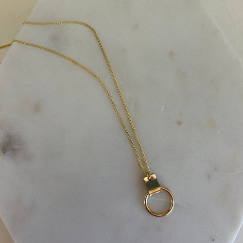 Gold metal chain with a metal ring pendent. Flat laid on a marble white background. 