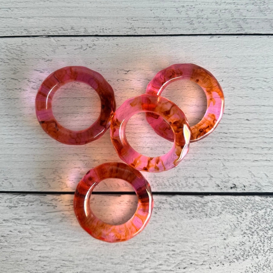Set of pink and orange acrylic napkin rings on a wooden surface