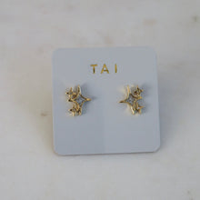 Load image into Gallery viewer, Pair of gold-plated starburst stud earrings featuring clear crystal details, mounted on a light gray TAI card and on a white surface.