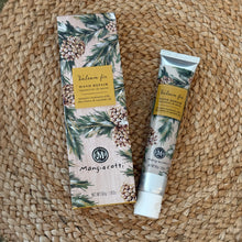 Load image into Gallery viewer, Balsam &amp; Fir, lifestyle image showing an overhead view of a silver-tone hand cream tube with a white cap beside its matching rectangular box, both featuring beige backgrounds, green evergreen branches, brown pinecones, and gold-colored panels with the scent name and product type in dark lettering, resting on a brown woven mat.