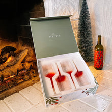 Load image into Gallery viewer, Set of four hand-blown crystal wine glasses with a red-to-white gradient design displayed inside an open Byrdeen gift box with a moss-colored lid, set on a white brick hearth beside a lit fireplace, a bottle of wine, and a small frosted holiday tree. 