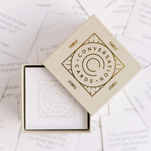 Load image into Gallery viewer, Cream box with a gold foil print that reads &quot;Conversation Cards&quot;. The box is opened and inside is a stack of white cards with a similar cream print. The box is on a background of the cards spread out. 