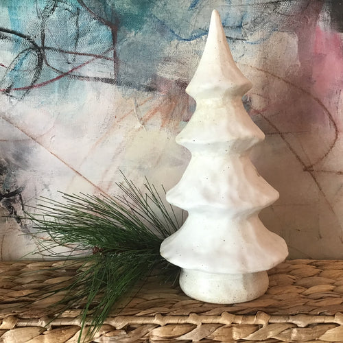 White ceramic Christmas tree on a wicker platform with a pine sprig behind it. Abstract background. 