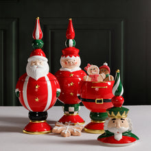 Load image into Gallery viewer, Three hand-painted ceramic cookie jars in festive holiday designs, including Santa Claus, Mrs. Claus, and a nutcracker in red outfits displayed together on a white surface. The nutcracker jar is shown with its lid off, revealing gingerbread cookies inside and a star-shaped cookie placed in front.     
