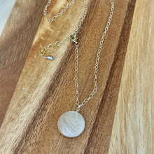 Load image into Gallery viewer, Gold chained necklace with a round mother of pearl pendant on a wooden surface.