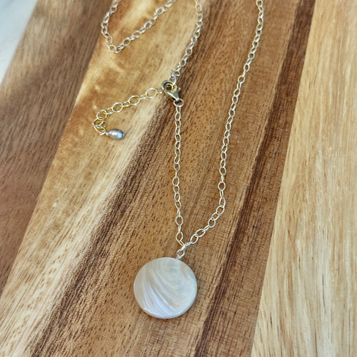 Gold chained necklace with a round mother of pearl pendant on a wooden surface.