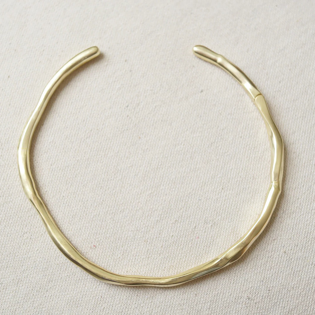 14K gold double semi-matte plated brass choker necklace with a gently, uneven, organic shape displayed on a cream woven fabric surface.