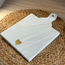 Load image into Gallery viewer, White marble serving board featuring a brass heart inlay, displayed on a woven placemat.