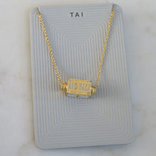 Load image into Gallery viewer, Back view of a gold-plated chain necklace and spinner pendant with the text "AND BACK," on a light gray TAI jewelry card, displayed on a white background. 