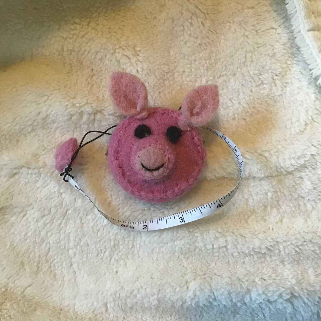 Pink pig felt measuring tape on a beige carpet.