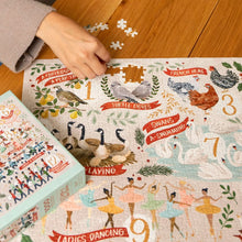 Load image into Gallery viewer, Partially assembled 12 Days of Christmas 1000 piece jigsaw puzzle on a wooden table with a hand placing pieces and the illustrated box resting beside it.