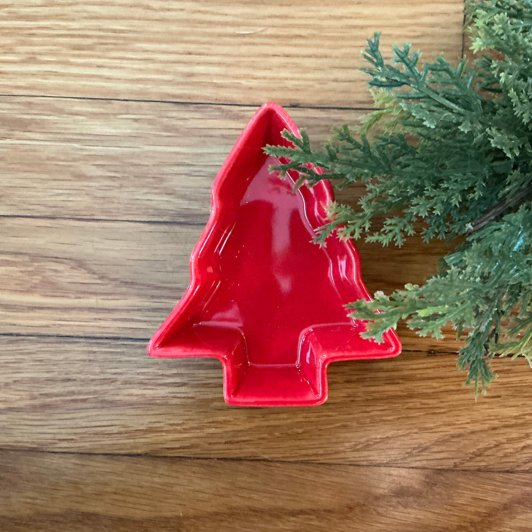 Red stoneware tree-shaped bowl on a wooden surface with greenery on the right side. 