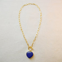 Load image into Gallery viewer, Gold-plated brass chain necklace with a large blue lapis stone pendant and a toggle closure, displayed on a textured cream surface. 