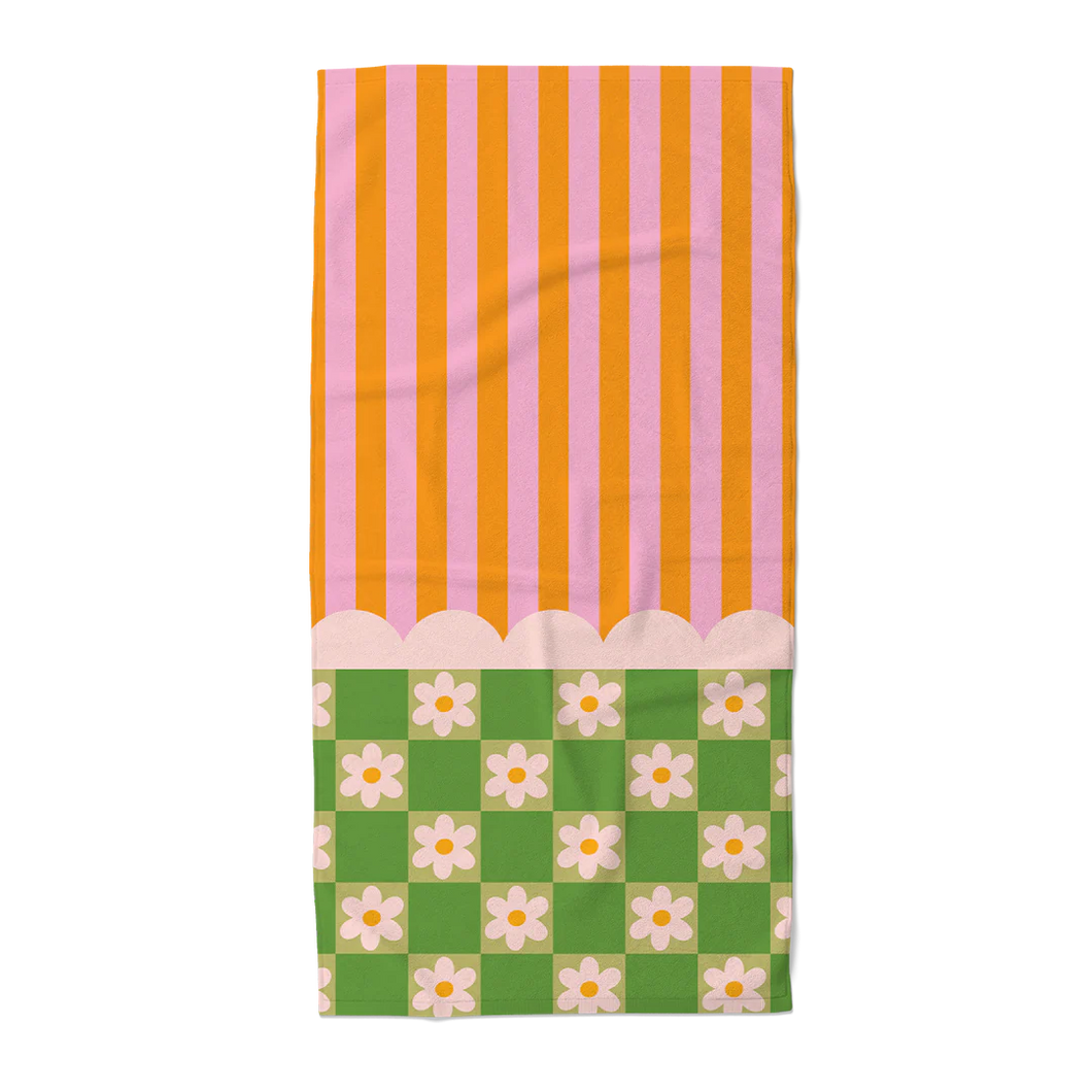Beach towel with an orange and pink striped top and a green and white floral checkered patterned bottom, separated by a white scalloped design. On a black and gray checkered background.